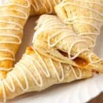 Apple turnovers drizzled with icing and stacked on a plate.