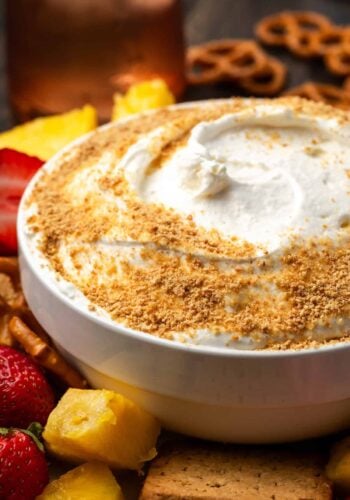 A bowl of cheesecake dip garnished with graham cracker crumbs surrounded by fresh fruit.