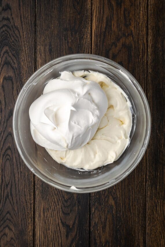 Whipped cream added to cheesecake dip ingredients in a bowl.