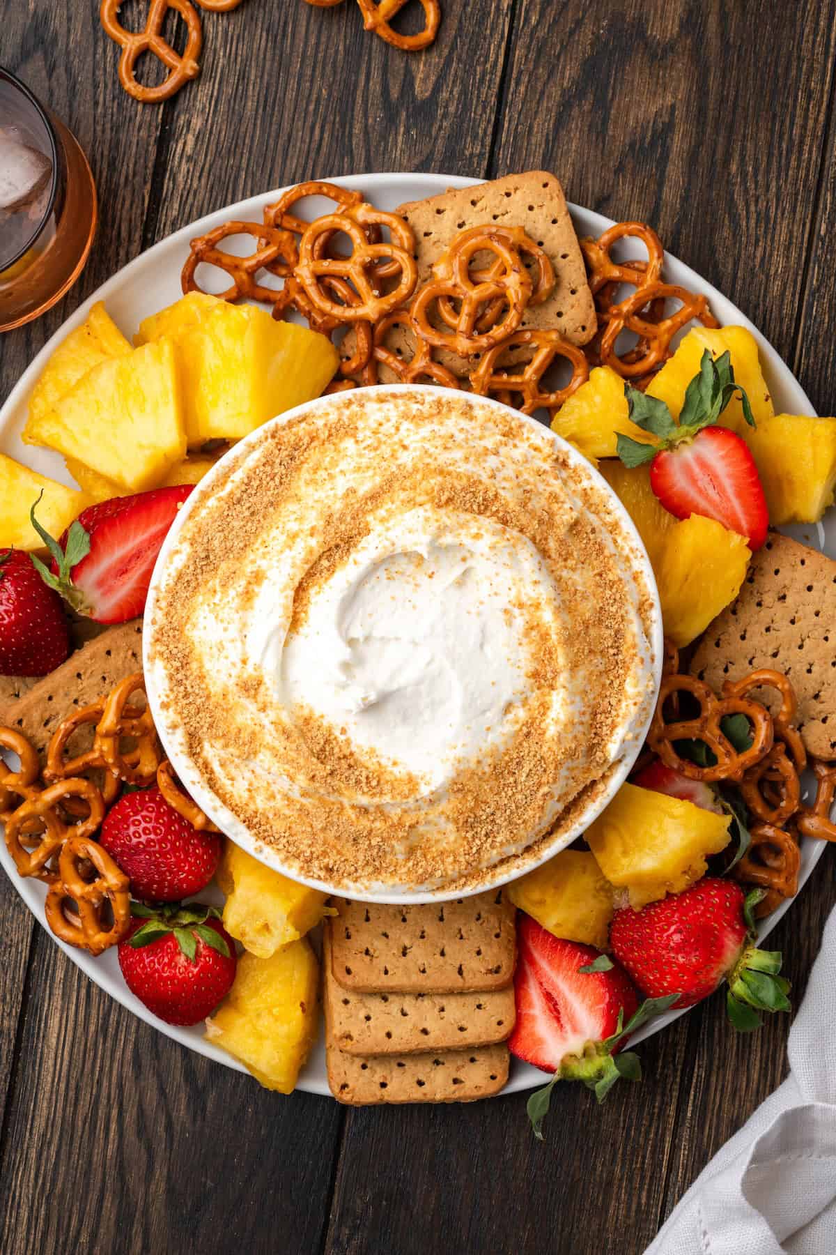 Overhead view of a bowl of cheesecake dip garnished with graham cracker crumbs in the center of a large platter of fresh fruit, pretzels, and graham crackers.