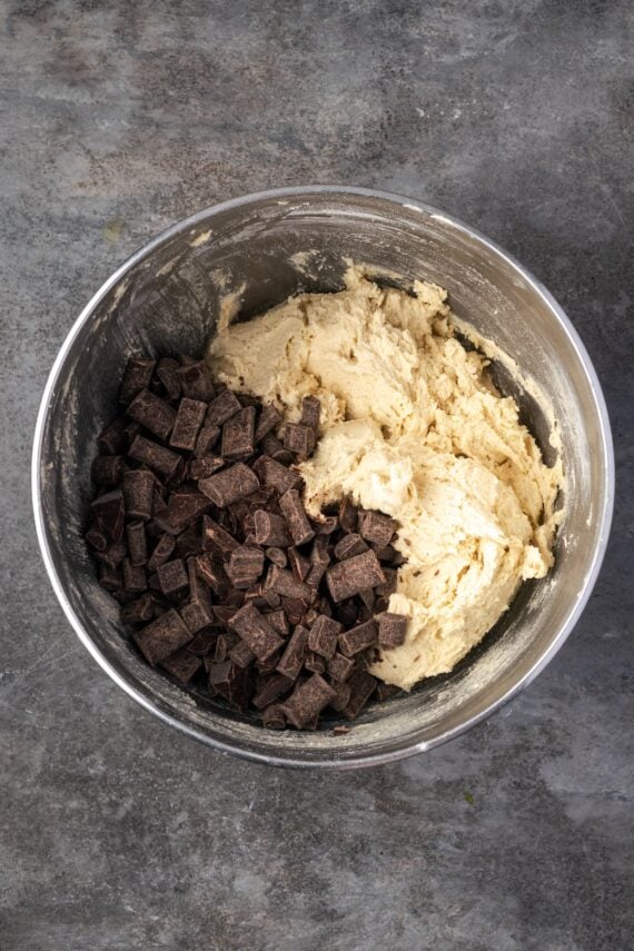 Chocolate chips added to cookie dough in a mixing bowl.