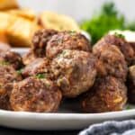 Side view of air fryer meatballs piled on a white serving platter.