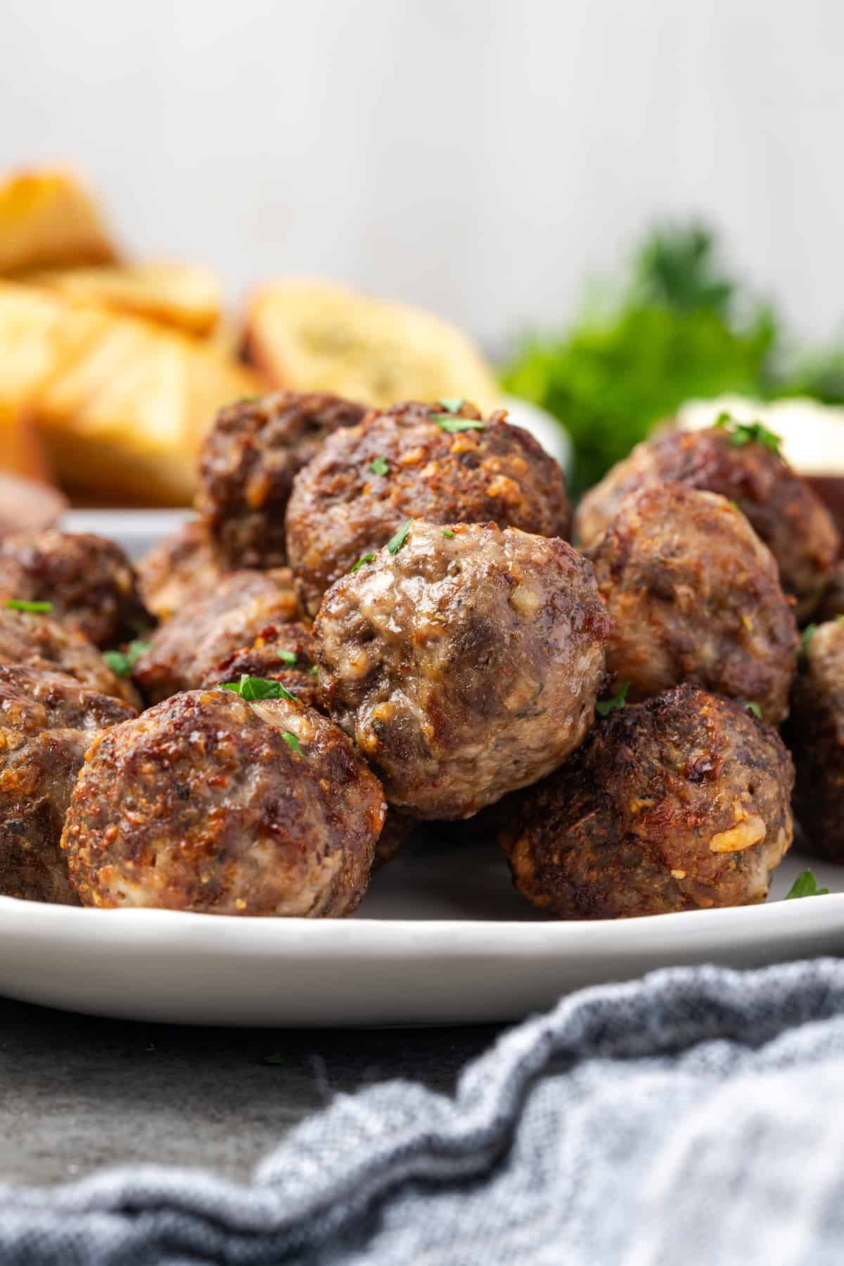 Side view of air fryer meatballs piled on a white serving platter.
