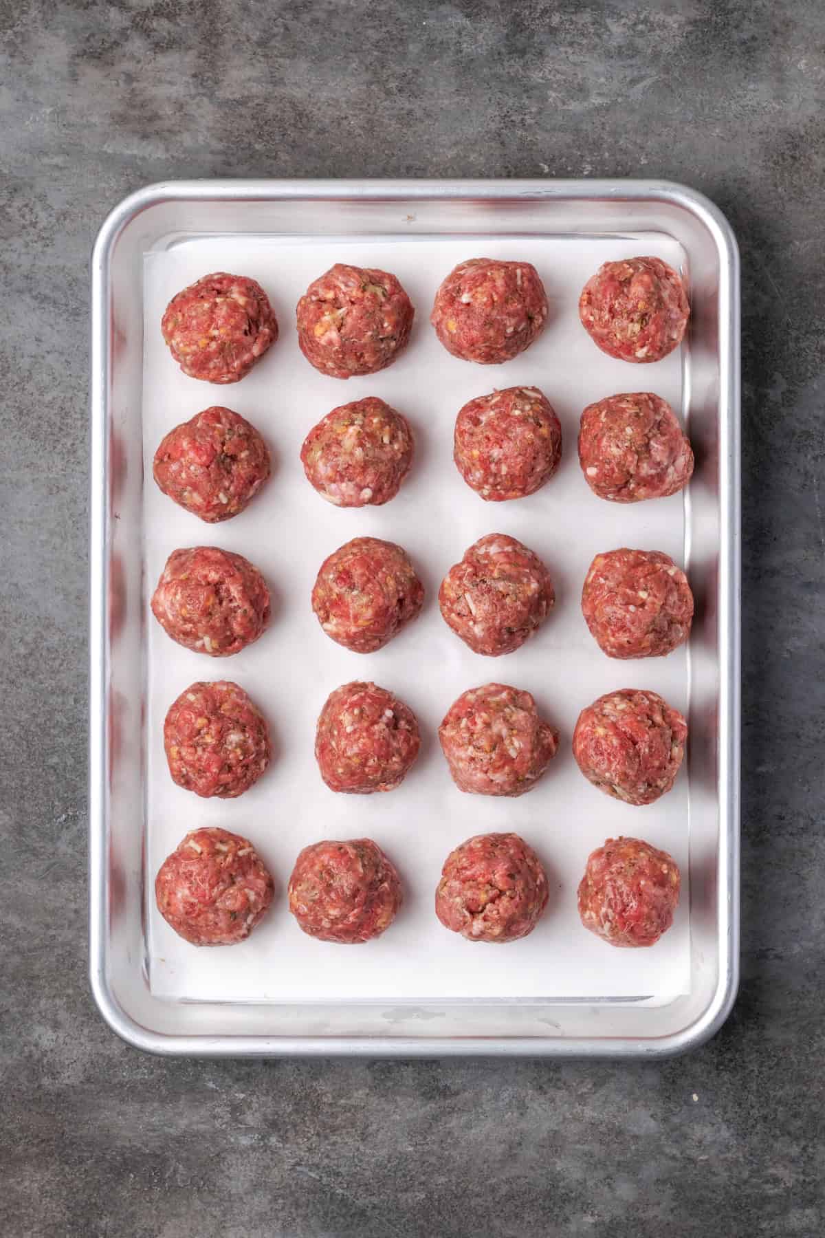 Raw meatballs arranged in rows on a baking sheet.