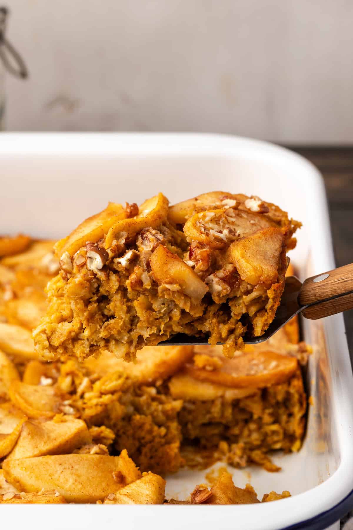 A slice of baked pumpkin oatmeal being lifted from a baking dish.