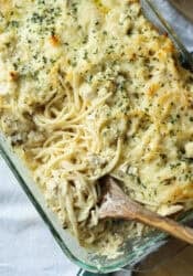Overhead view of a wooden spoon resting in a glass baking dish of chicken tetrazzini.