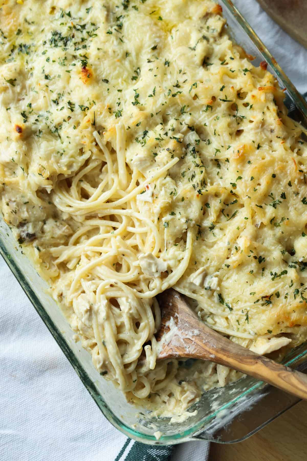Creamy chicken tetrazzini is an easy pasta bake that's ready in under an hour! Made with juicy chicken and spaghetti in a rich cream sauce. Overhead view of a wooden spoon resting in a glass baking dish of chicken tetrazzini.