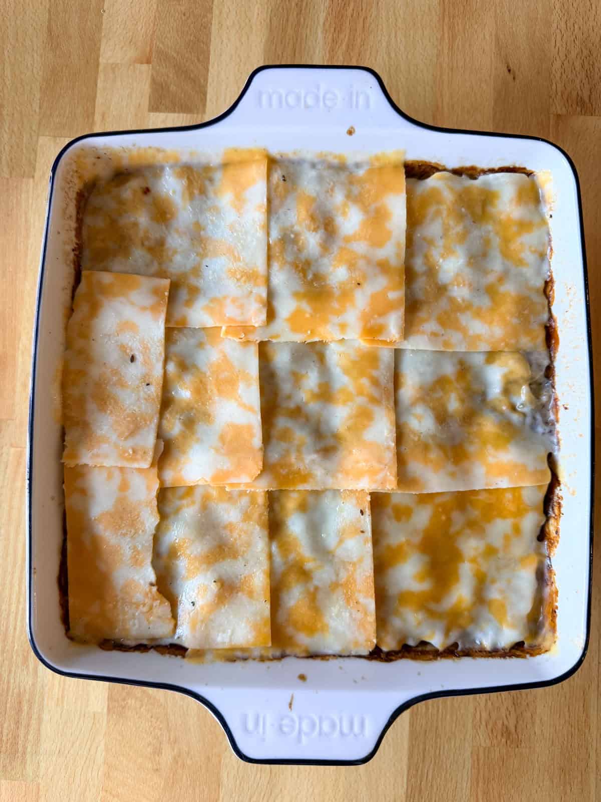 Cheese slices on top of a hamburger casserole beginning to melt before being placed back in the oven.