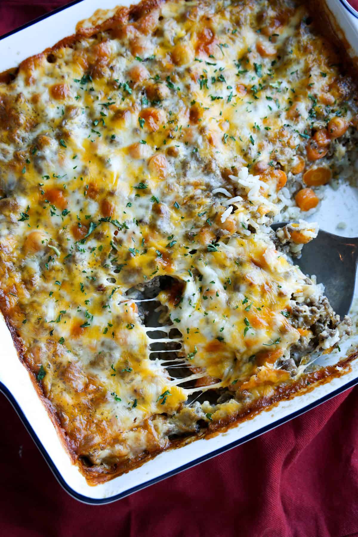 Ground Beef Casserole topped with melted cheese and serving it with a spoon.