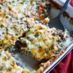 Cheese topped rice and ground beef casserole baked in a white ceramc baking dish with a spoon serving a piece