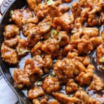 Close up of copycat PF Chang's spicy chicken in a skillet with a wooden spoon.