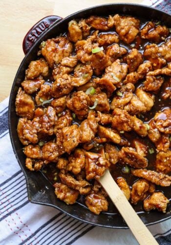 Overhead view of copycat PF Chang's spicy chicken in a skillet with a wooden spoon.