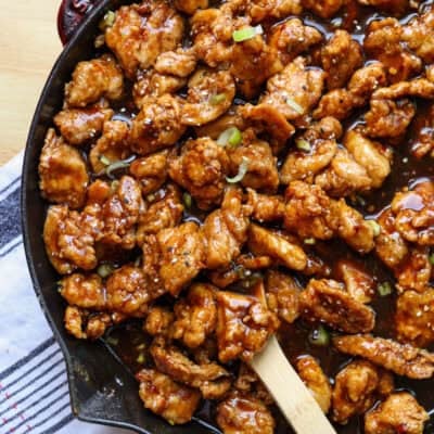 Overhead view of copycat PF Chang's spicy chicken in a skillet with a wooden spoon.