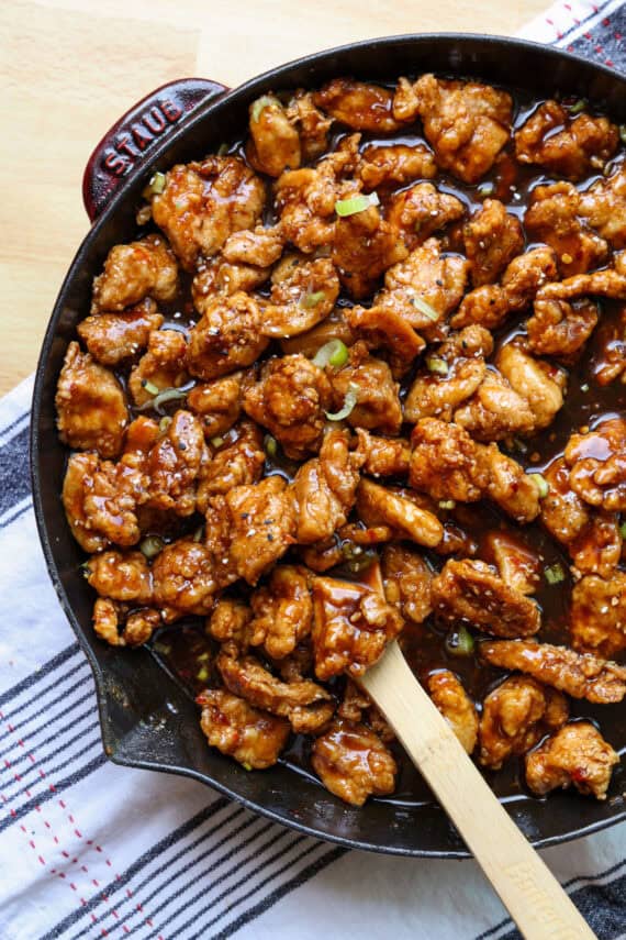 Overhead view of copycat PF Chang's spicy chicken in a skillet with a wooden spoon.