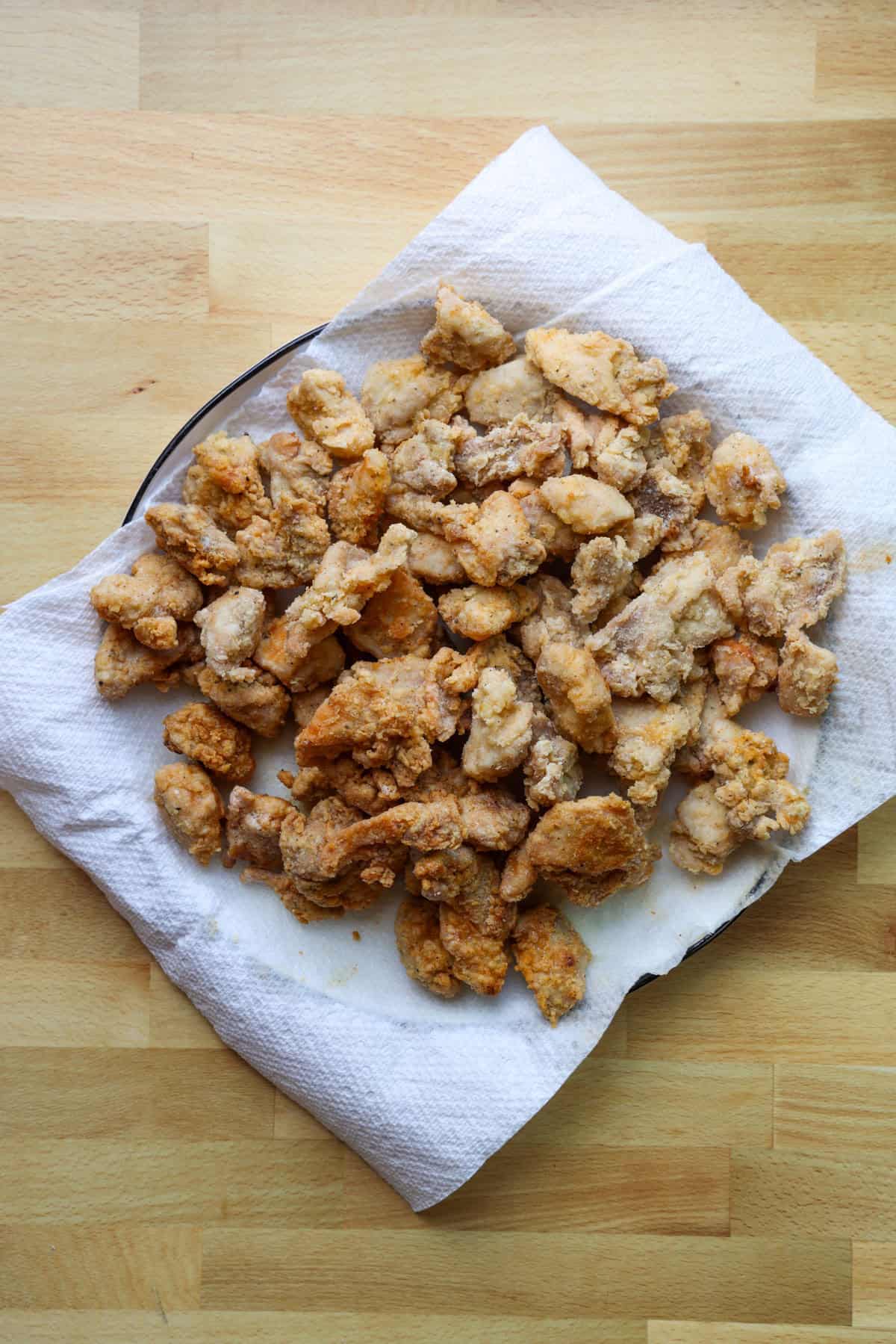 This copycat PF Chang’s spicy chicken recipe is a quick and delicious sweet and spicy stir-fry! Make it in one skillet and serve it with rice. Crispy fried chicken pieces draining on a paper-towel-lined plate.