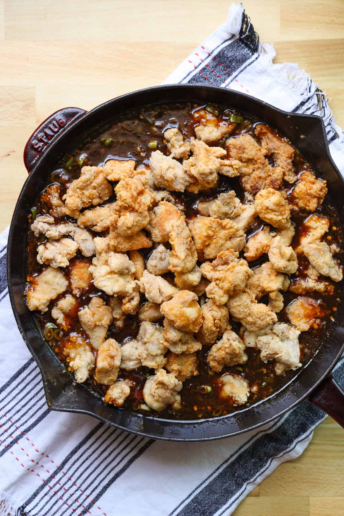This copycat PF Chang’s spicy chicken recipe is a quick and delicious sweet and spicy stir-fry! Make it in one skillet and serve it with rice. Overhead view of fried chicken pieces added to sweet and spicy stir-fry sauce in a skillet.