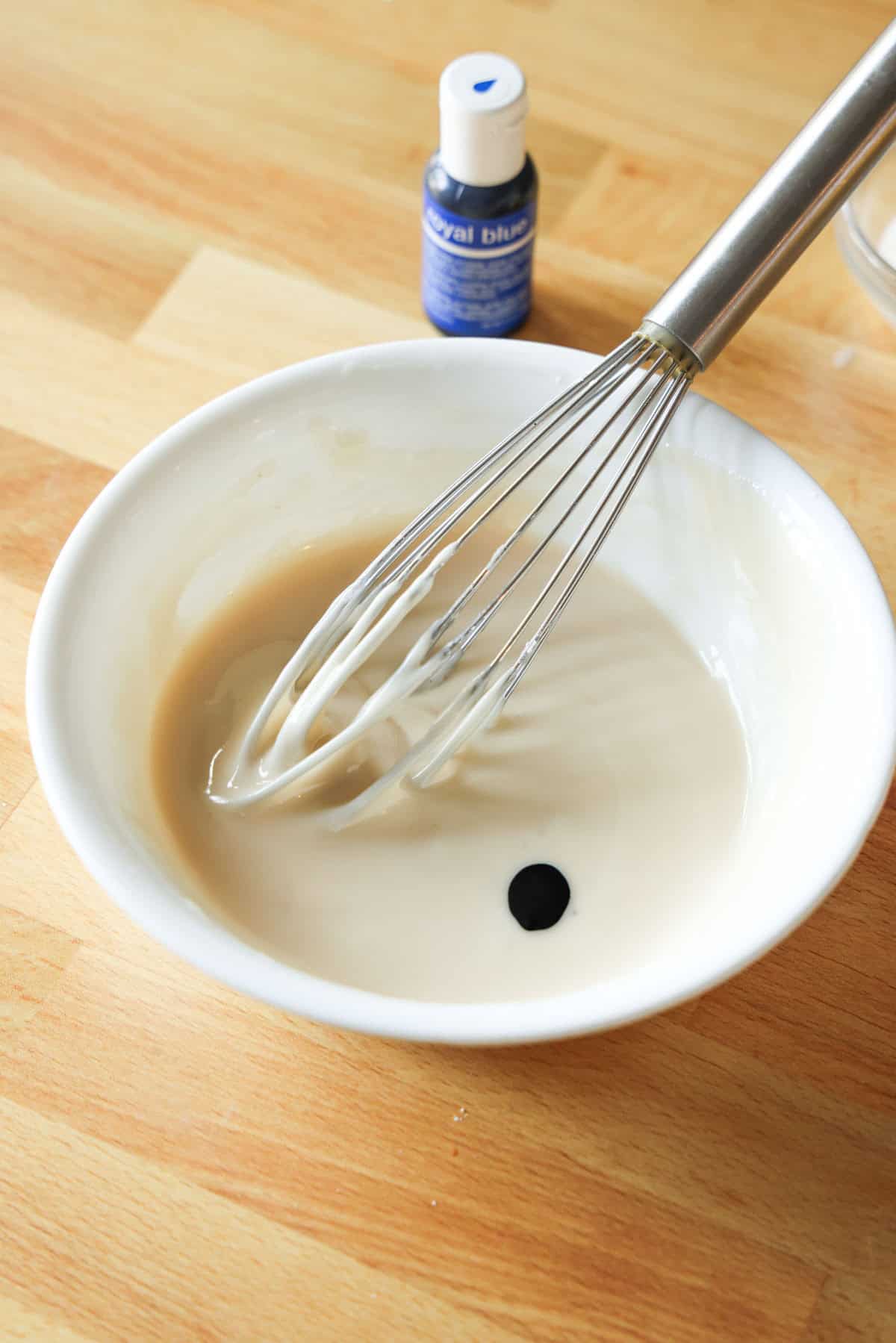 A drop of blue gel food coloring added to a bowl of sugar cookie icing.