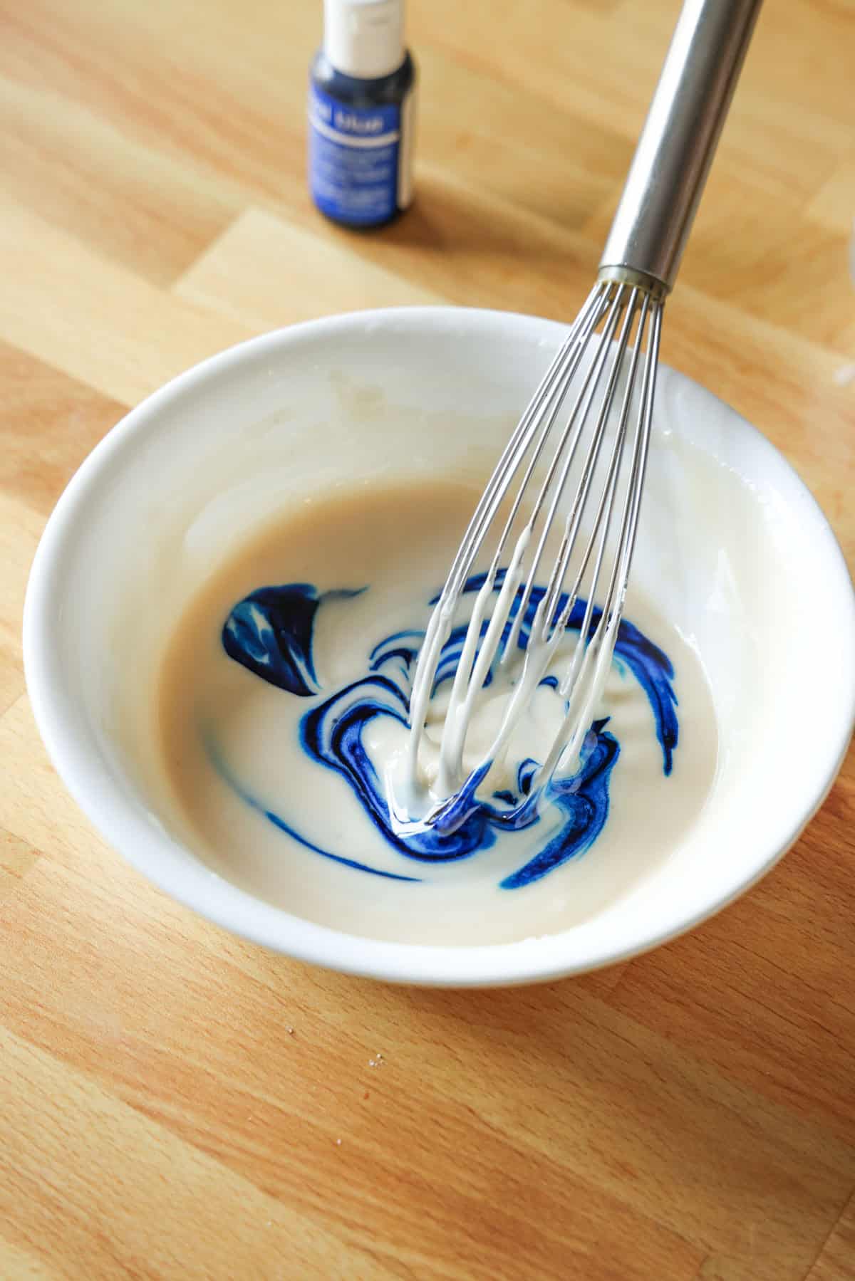 Blue gel food coloring partially whisked into a bowl of sugar cookie icing.