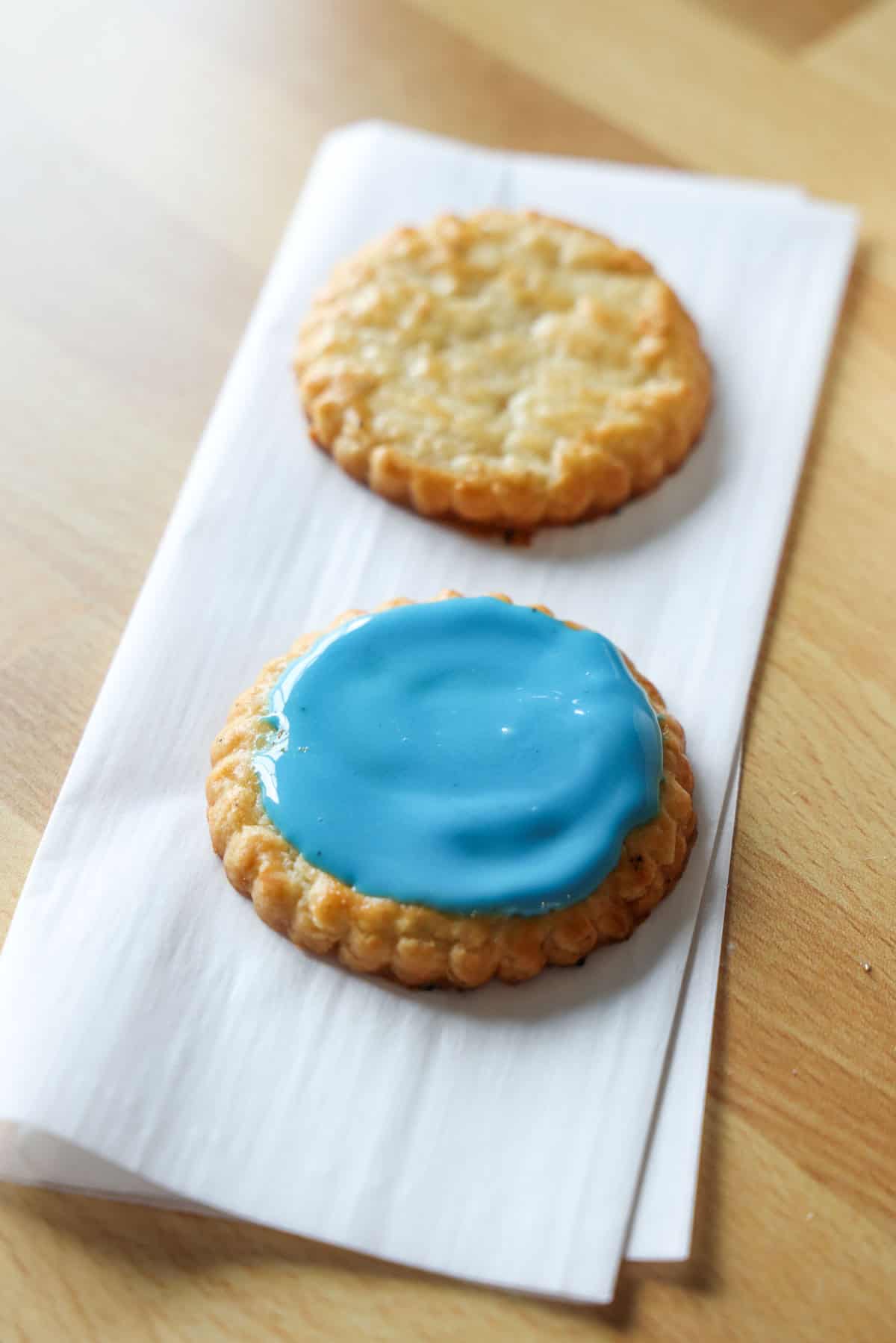 Close up of a sugar cookie topped with blue sugar cookie icing with a second unfrosted cookie in the background.