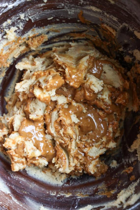 Melted Biscoff spread swirled into cookie dough in a mixing bowl.