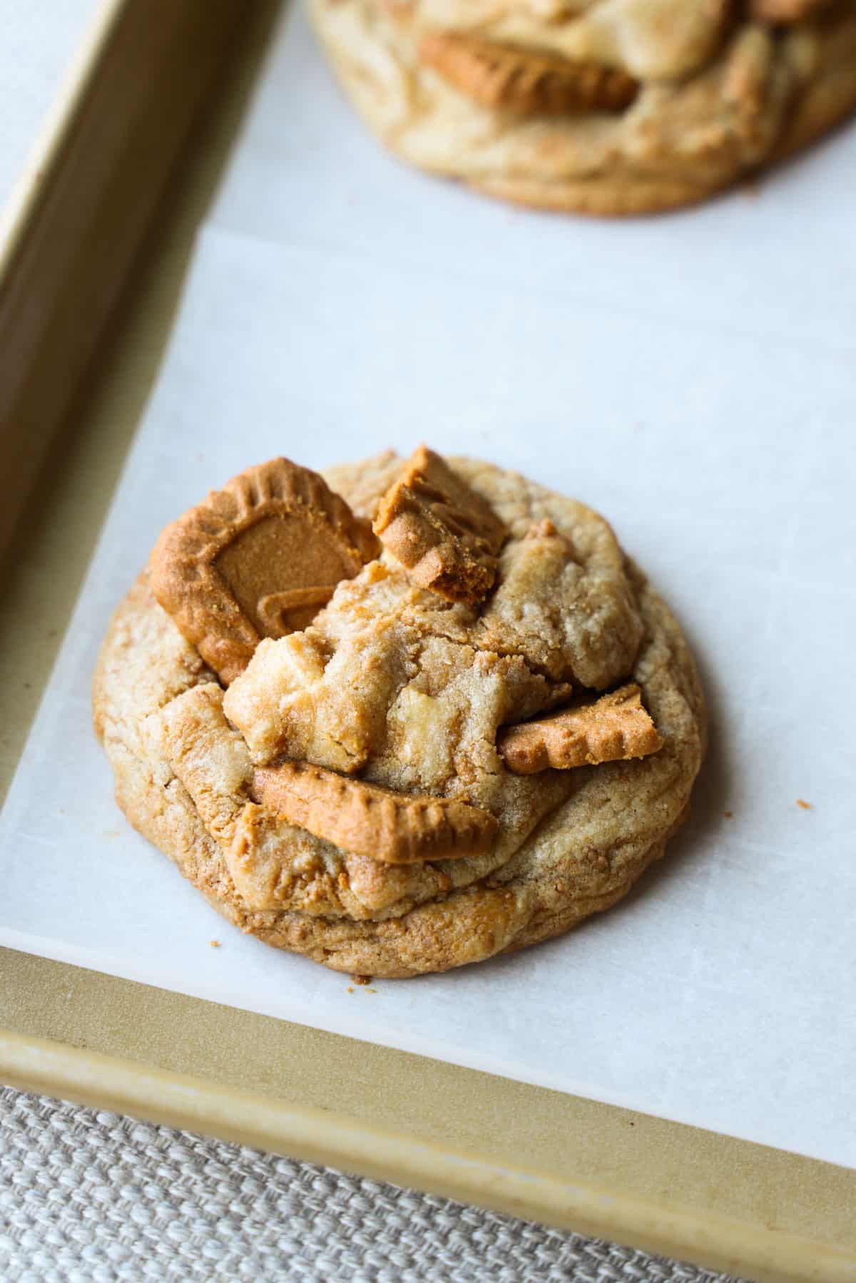 These absolutely delicious Stuffed Biscoff (Cookie Butter) Cookies are easy to make and are certain to impress. Filled and swirled with gooey Biscoff spread! A baked Biscoff Stuffed cookie on a parchment lined baking sheet with pieces of broken Biscoff pressed on top.
