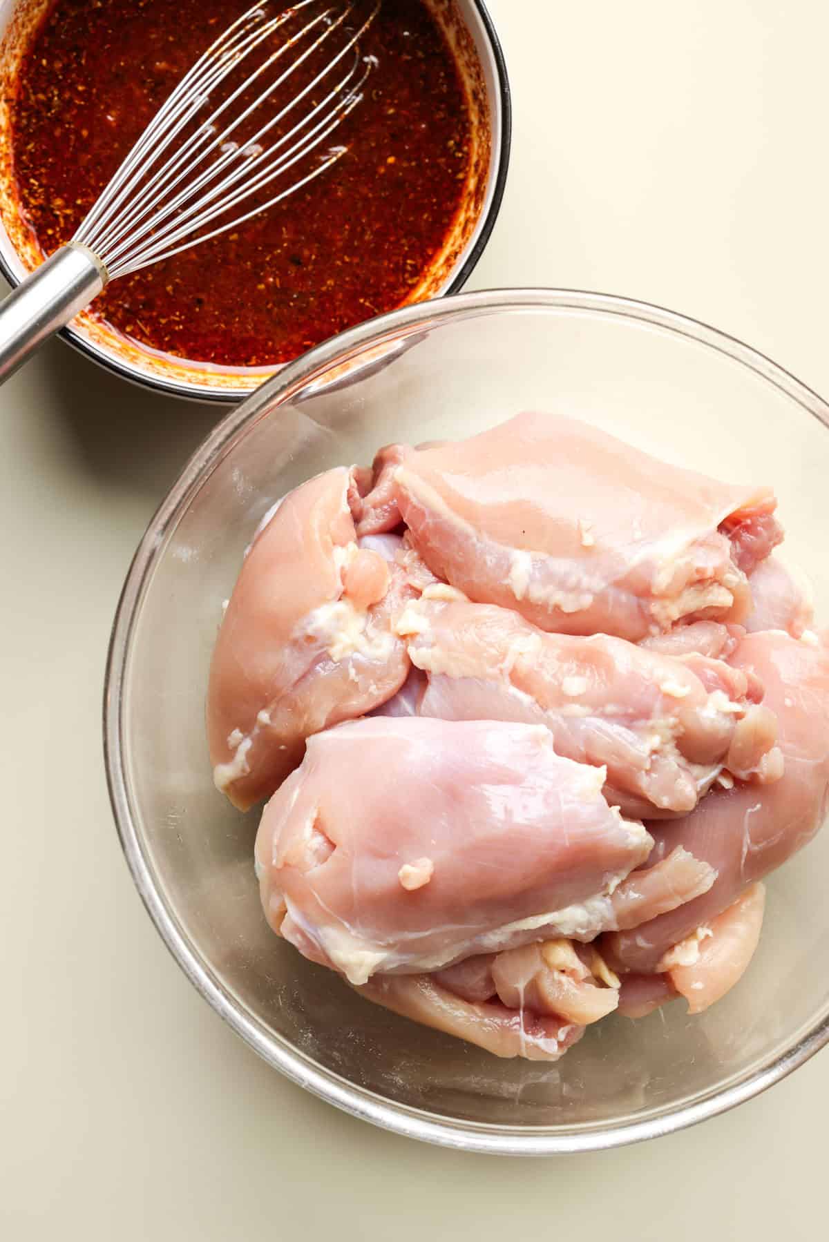 Chicken thighs in a glass bowl next to a smaller bowl of Chipotle chicken marinade.
