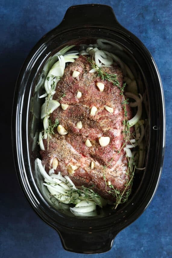 Pork shoulder combined with onions, garlic, and seasonings in the slow cooker.