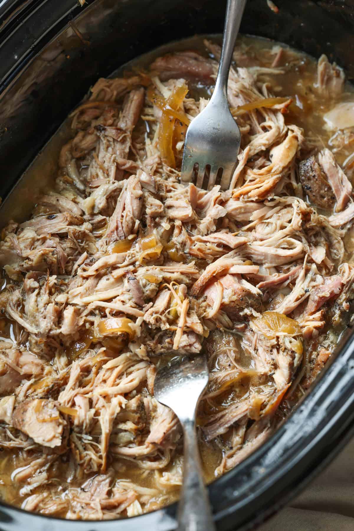 This crock pot pulled pork recipe makes the best sliders! Juicy pork shoulder is slow-cooked with apple marinade until it's fall-apart-tender. Overhead view of pulled pork inside the crock pot.