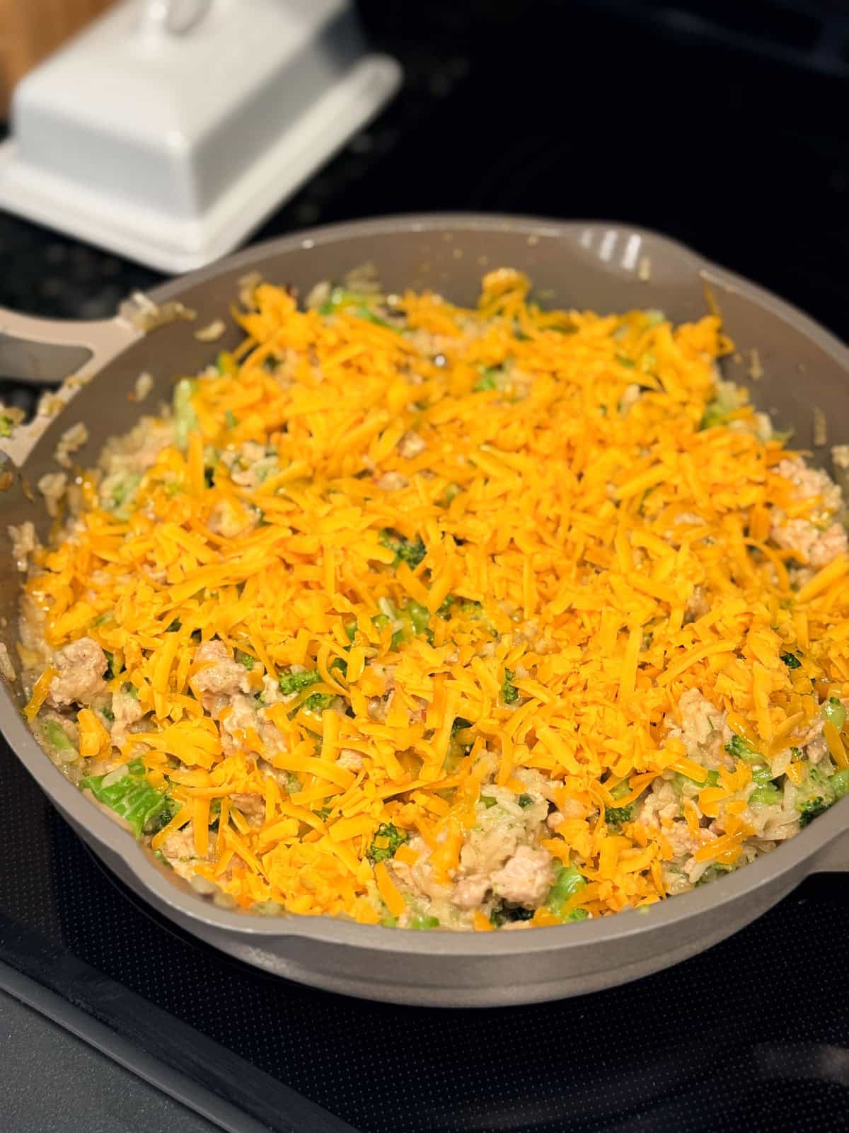 Shredded cheese added on top of creamy chicken broccoli and rice in a skillet.