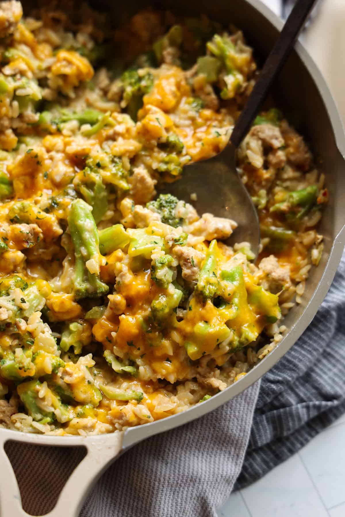 A spoon scooping cheesy chicken and broccoli with rice from a skillet.
