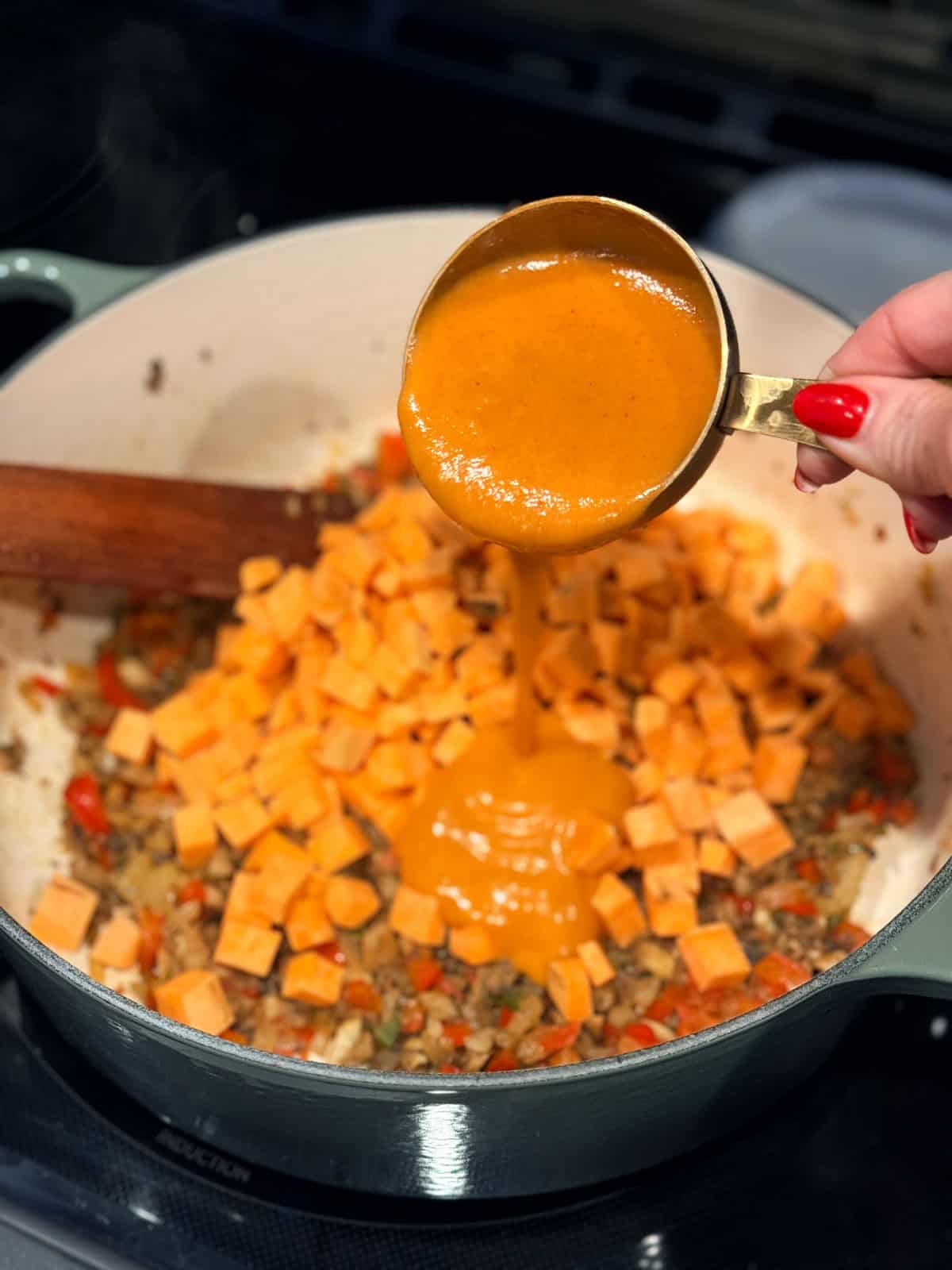 This coconut curry soup has tender Chinese potstickers swimming in a rich coconut broth with veggies. Ready in one pot in under an hour! Red curry paste being added to a pot with diced vegetables.