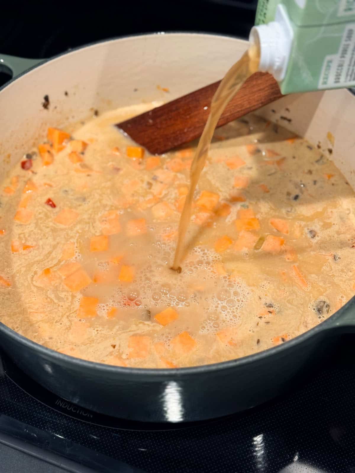 This coconut curry soup has tender Chinese potstickers swimming in a rich coconut broth with veggies. Ready in one pot in under an hour! Broth being poured into a pot of coconut curry soup ingredients.