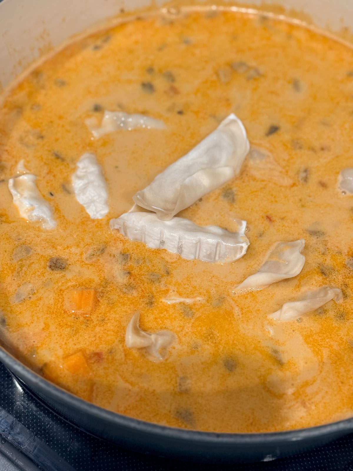 This coconut curry soup has tender Chinese potstickers swimming in a rich coconut broth with veggies. Ready in one pot in under an hour! Potstickers added to a pot of coconut curry soup.