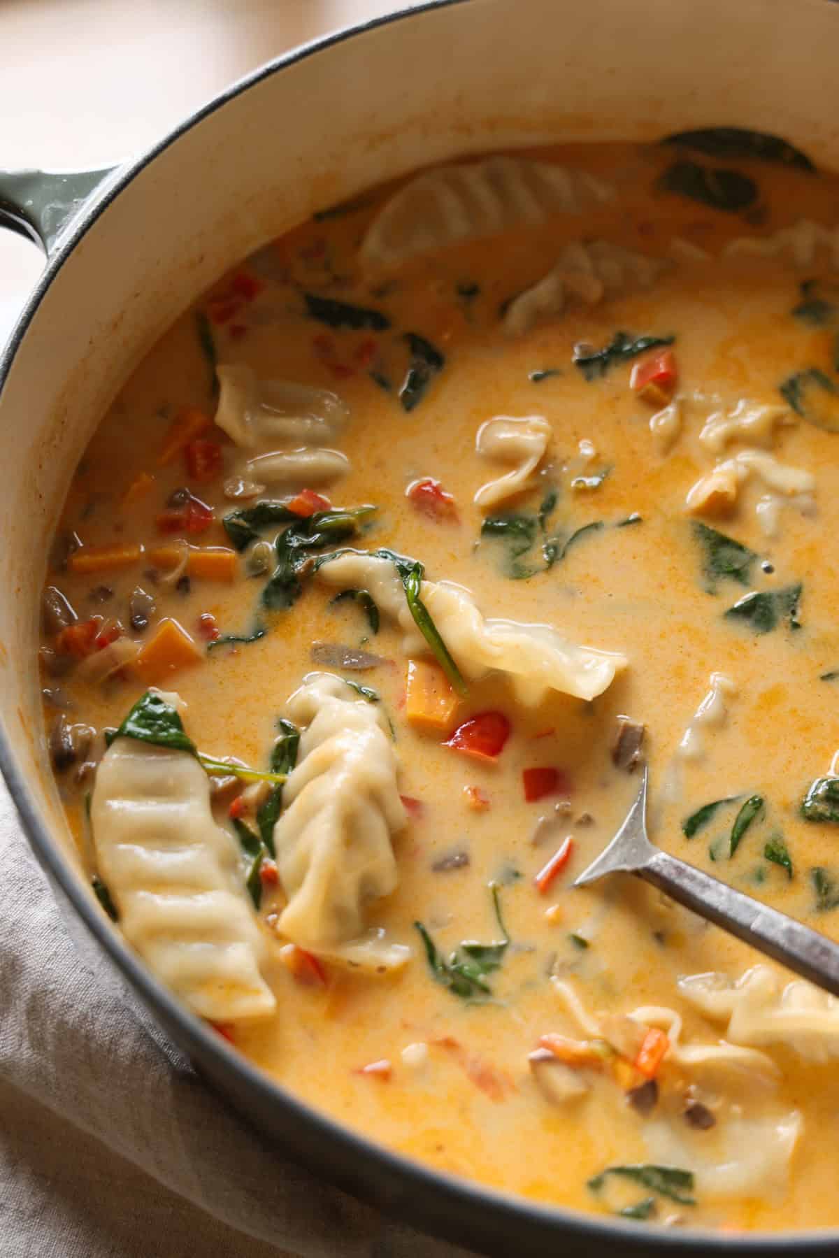 This coconut curry soup has tender Chinese potstickers swimming in a rich coconut broth with veggies. Ready in one pot in under an hour! Coconut curry soup with potstickers in a large pot.