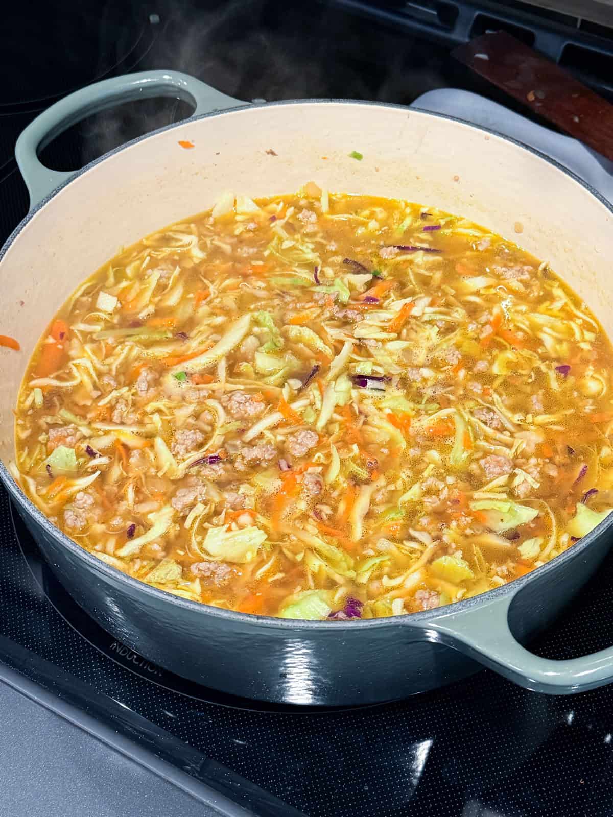 This easy egg roll soup has all the Asian-inspired flavors you love, with juicy ground pork simmered with tender cabbage, sesame, and ginger. Egg roll soup inside a Dutch oven.