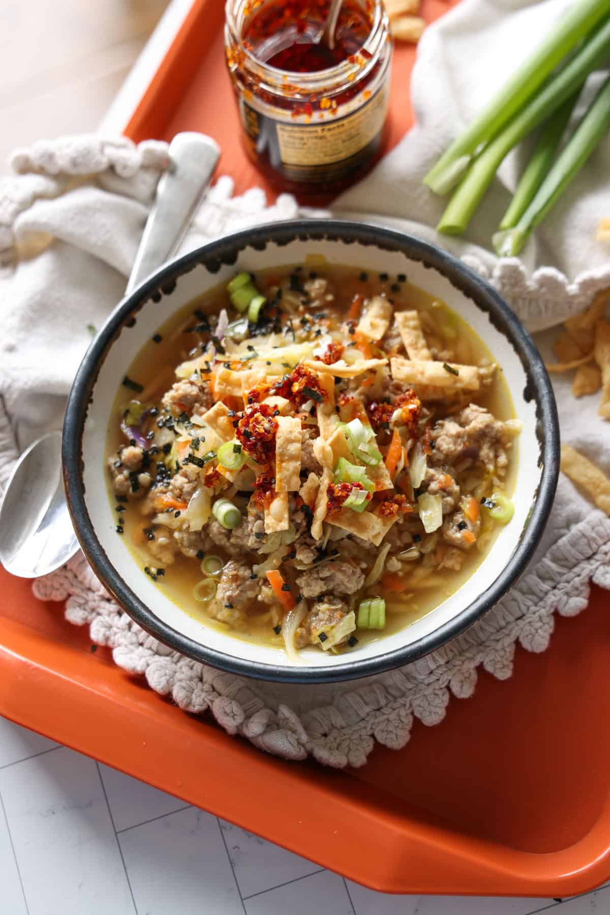 This easy egg roll soup has all the Asian-inspired flavors you love, with juicy ground pork simmered with tender cabbage, sesame, and ginger. Overhead view of a bowl of egg roll soup garnished with green onions and crispy wonton strips.