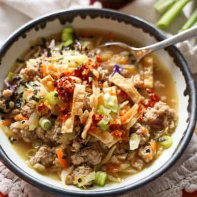 Overhead view of a spoon dipped into a bowl of egg roll soup garnished with green onions and crispy wonton strips.