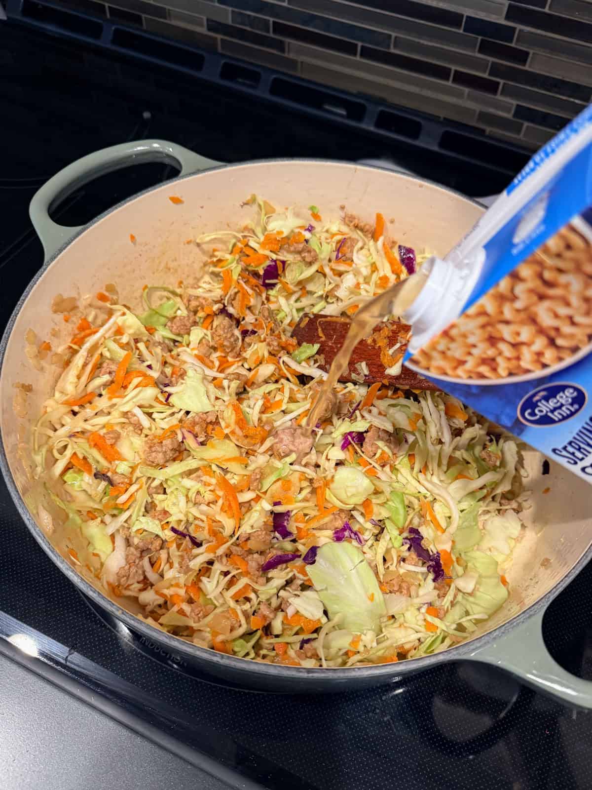 This easy egg roll soup has all the Asian-inspired flavors you love, with juicy ground pork simmered with tender cabbage, sesame, and ginger. Chicken stock being poured over egg roll soup ingredients in a Dutch oven.