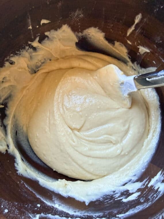 Once the cakes have baked, cool them and then level them off if domes have formed (if necessary). Use a serrated knife to slice the cakes in half. Lemon Cake batter in a wooden bowl