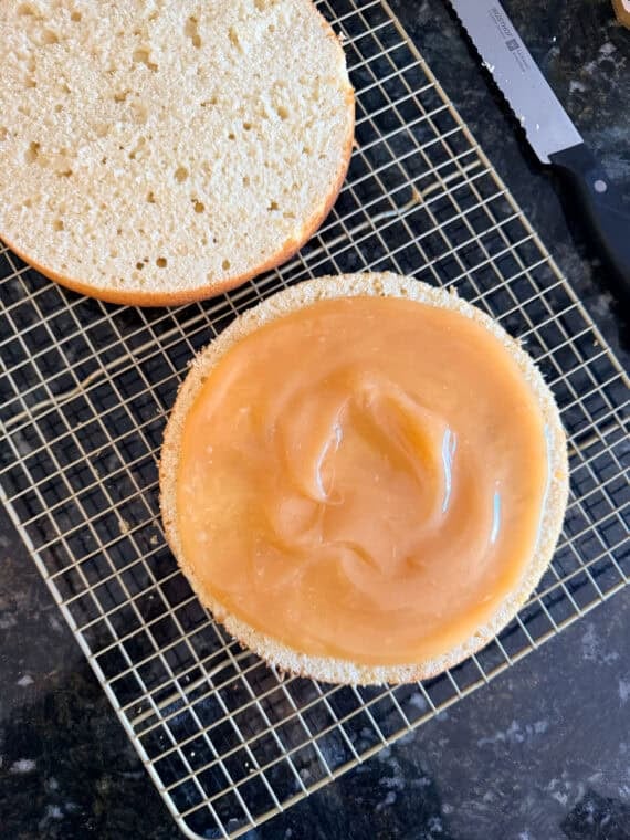Once the cakes have baked, cool them and then level them off if domes have formed (if necessary). Use a serrated knife to slice the cakes in half. Lemon Curd spread on top of a lemon cake to layer.