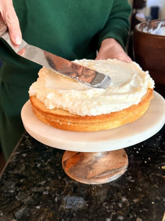 Once the cakes have baked, cool them and then level them off if domes have formed (if necessary). Use a serrated knife to slice the cakes in half. Spreading buttercream frosting on a layer cake with an offset spatula