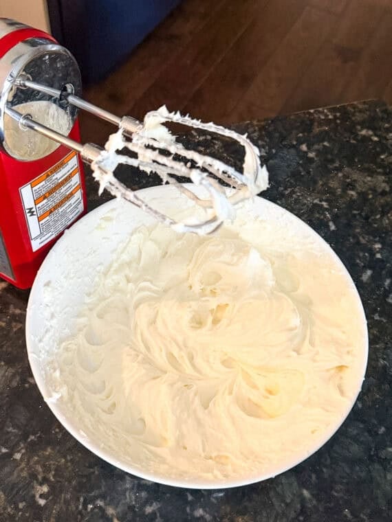 A bowl of cream cheese and sugar mixed together using an electric hand mixer.