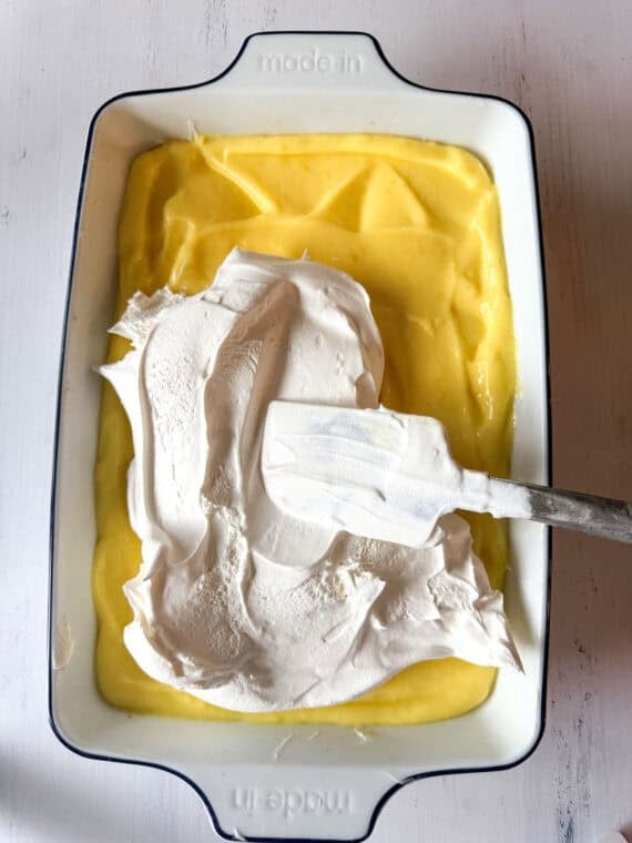 Spreading whipped topping on top of lemon pudding in a 9x13 pan for a layered lemon dessert.