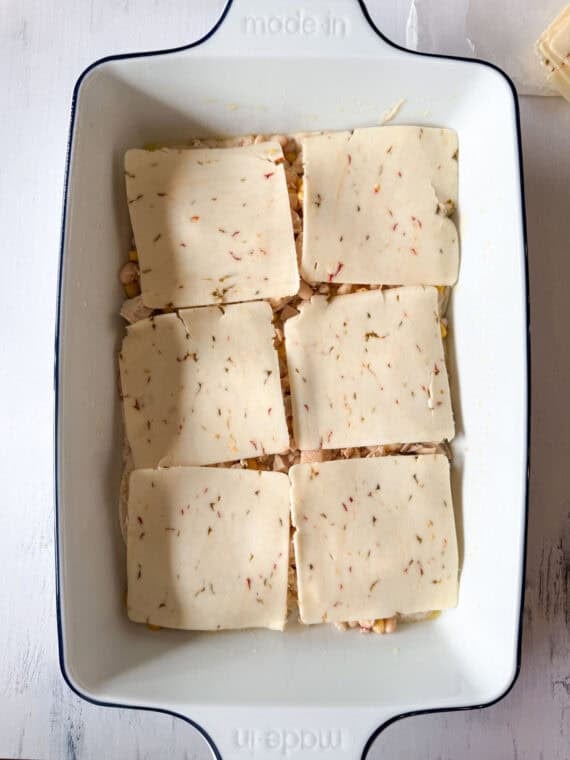 This Chicken Enchilada Casserole is going to earn a regular spot on your menu. It has all the cozy flavors of classic chicken enchiladas layered into an easy casserole Slices of pepper jack cheese layered in a white ceramin baking dish.