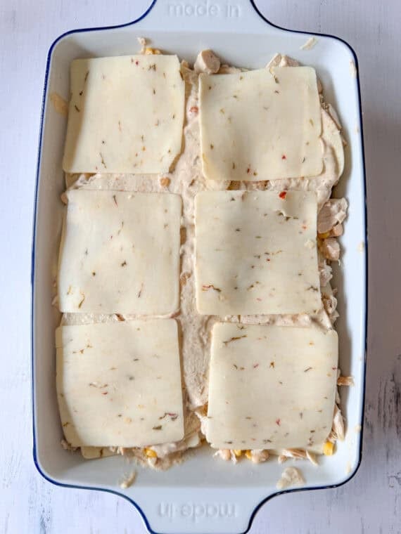 This Chicken Enchilada Casserole is going to earn a regular spot on your menu. It has all the cozy flavors of classic chicken enchiladas layered into an easy casserole Cheese slices on top of a casserole before going in the oven.