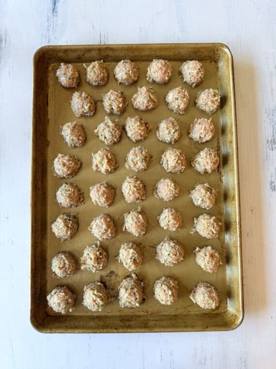 Chicken meatball mixture scooped on a baking sheet before going into the oven