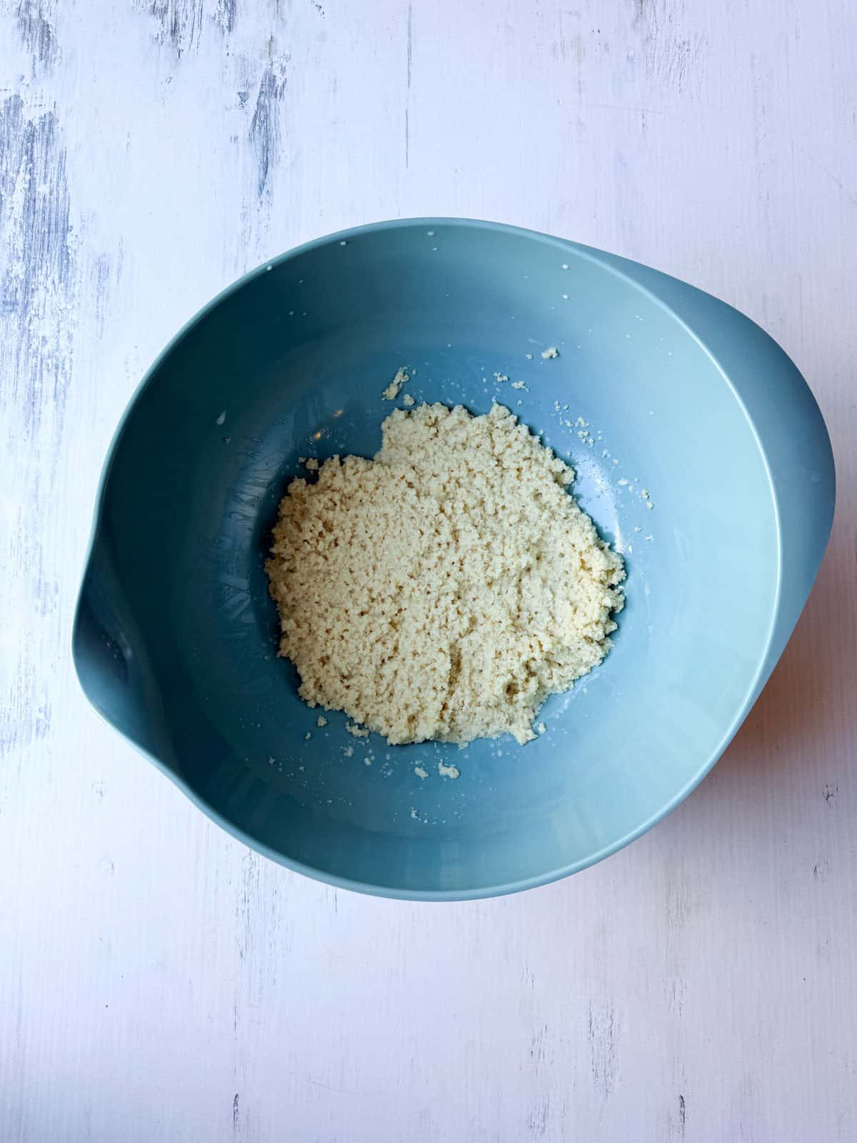 Panko breadcrumbs being soaked in milk making a panade in a blue bowl.