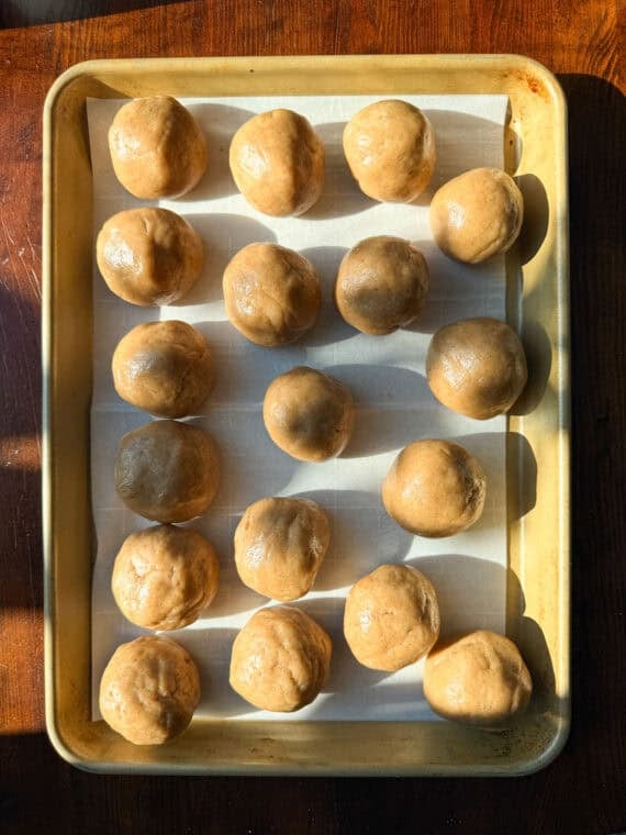 Cookie dough balls on a parchment lined baking sheet.