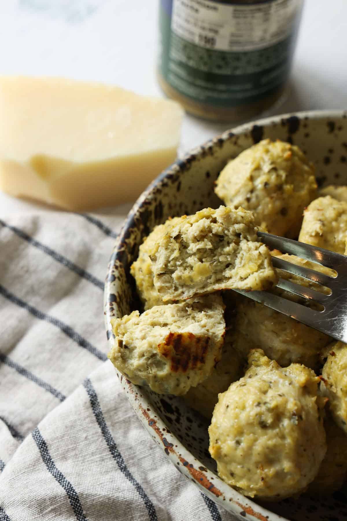 These juicy Pesto Chicken Meatballs are packed with fresh basil flavor, plenty of Parmesan cheese, and come together with just a handful of simple ingredients. They're baked instead of fried and ready in about 30 minutes making them an easy weeknight dinner or meal prep and packed with protein! A fork holding half of a pesto meatball, showing the soft interior.