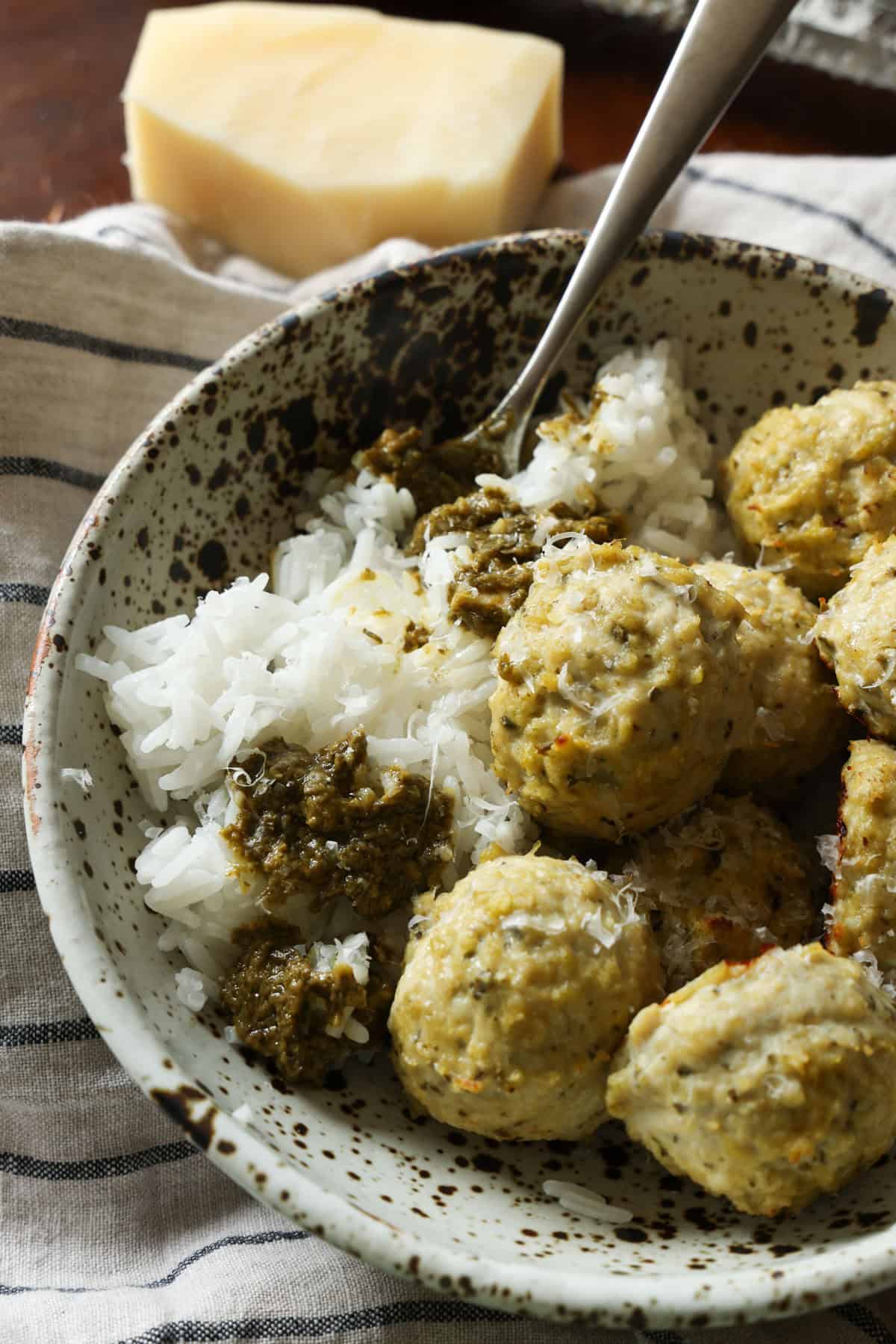 These juicy Pesto Chicken Meatballs are packed with fresh basil flavor, plenty of Parmesan cheese, and come together with just a handful of simple ingredients. They're baked instead of fried and ready in about 30 minutes making them an easy weeknight dinner or meal prep and packed with protein! Chicken Pesto meatballs in a bowl with white rice and more pesto sauce.